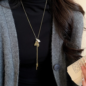 Close-up of golden leaf tassel pendant necklace styled over black sweater for women