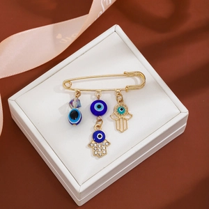 Detail of gold hamsa hand and blue evil eye charms on a tassel brooch pin