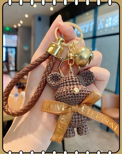 Detailed view of a brown resin bear keychain with a gold bell and woven PU strap