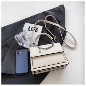 Close-up of cream flap handbag with silver chain detail and sleek black trim on suit