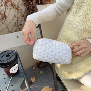 Lifestyle shot of a white quilted floral makeup bag held by hands at an outdoor cafe