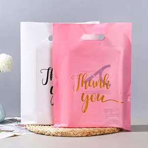 Pink and white plastic gift bags with gold 'Thank you' text and handles on straw mat