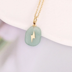 Macro shot of gold necklace with oval green stone pendant and lightning bolt inlay