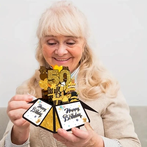 Smiling senior woman opening a 3D pop-up 50th birthday card box in gold and black