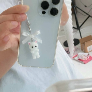 Cute white flocked kitten phone charm with pink ears and bow on a blue smartphone