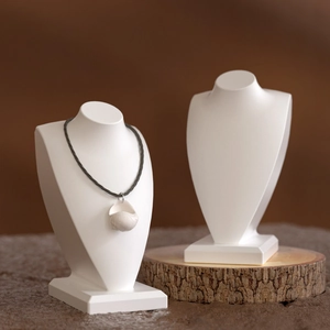 Detail view of matte white resin bust necklace displays on a rustic wooden base
