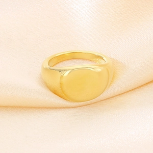 Primo piano di un anello a sigillo rotondo lucido placcato oro 18K su raso color champagne