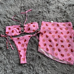 Detailed view of pink strawberry print 3-piece bikini set with a sheer mesh wrap skirt