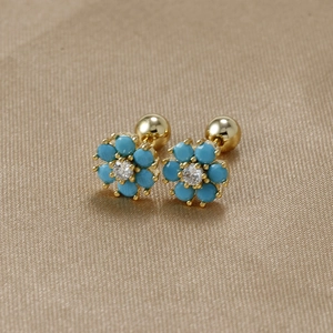 Macro shot of turquoise floral earrings with gold screw backs on textured fabric