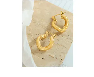 Macro shot of gold-plated twisted C-shaped titanium steel earrings on stone surface