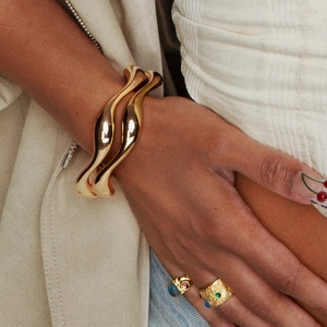 Bracelets ondulés dorés et bagues de pierres précieuses sur mannequin au style élégant