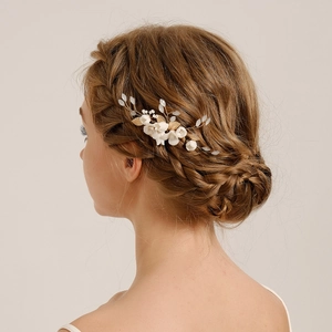 Detail of bridal hair comb with white ceramic flowers and golden leaves on braided hair