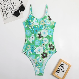 Flat lay of retro green floral one-piece swimsuit with daisy patterns and sunglasses