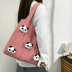 Red plaid canvas tote bag with 3D panda plush charms being worn as a shoulder bag