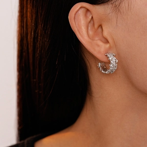 Close-up of sparkling silver zircon pavé C-shaped stud earrings on a model's ear