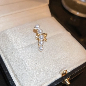 Macro detail of golden ear cuff with five white pearls on soft velvet jewelry box