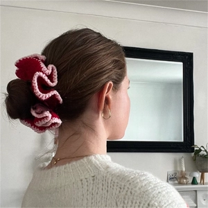 Detail of red and pink crochet ruffled scrunchie on a hair bun in a cozy home setting
