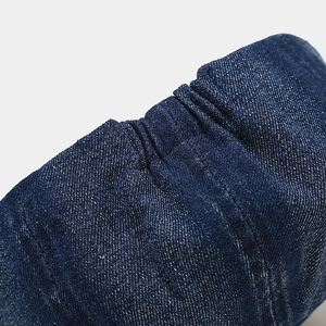 Detailed close-up of dark blue denim fabric with elastic pleats and white stitching