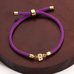 Macro shot of purple braided bracelet with gold-plated letter B pendant and zircons