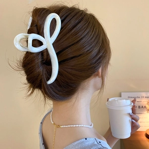 Detail of a large white cream bow hair claw clip featuring a pearlescent finish on hair