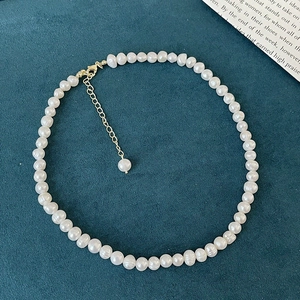 Detailed view of freshwater pearl necklace with gold lobster clasp on green fabric