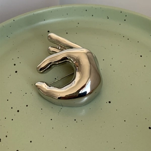 Vue détaillée d'une broche argentée en forme de main sur une assiette en céramique verte