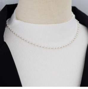 Detailed close-up of a delicate white pearl necklace with gold clasp on a model's neck