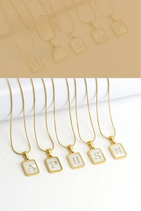 Detail of gold square pendant with white shell inlay and engraved capital letters necklace