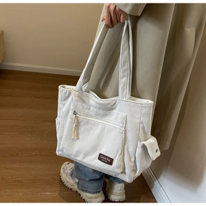 Close-up of off-white corduroy tote bag with fashion label held by a model