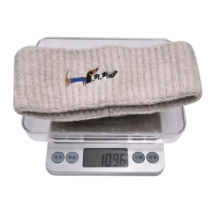Detail view of oatmeal knitted headband with dog embroidery showing weight on scale