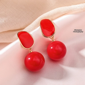 Détail de boucles d'oreilles pendantes rouges et dorées sur fond de satin champagne doux