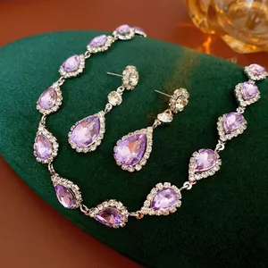 Elegant silver necklace and waterdrop earrings set with purple crystals on green velvet