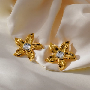 Detailed macro view of golden flower earrings featuring a square zircon center and silk texture