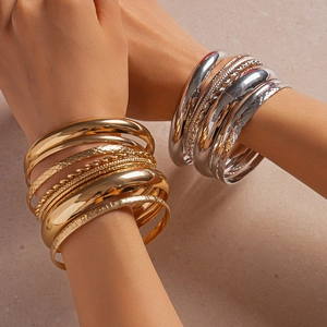 Detail of stacked metallic bangles with high-polish finish and textured geometric patterns