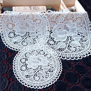 Close-up of white lace coasters with intricate rose patterns and wavy scalloped edges