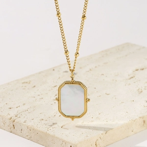 Vintage gold titanium steel necklace with rectangular white shell pendant on travertine