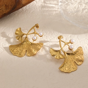 Detailed view of gold ginkgo leaf earrings featuring two white pearls on textured background