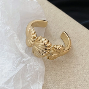Detailed close-up of a gold shell-shaped cuff bracelet with a layered fan relief design