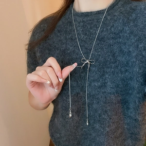 Close-up of silver bow pendant necklace styled on a charcoal grey knit sweater
