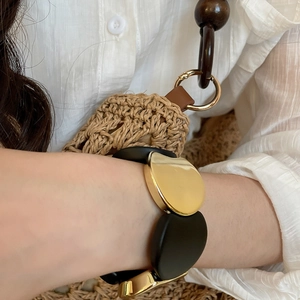 Detail of chunky black and gold acrylic stretch bracelet on woman's wrist with resort styling