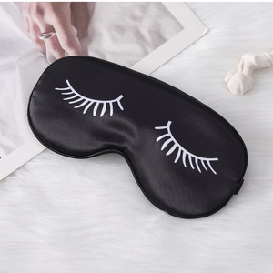Detail of silk satin black sleep mask featuring white eyelash print on plush background
