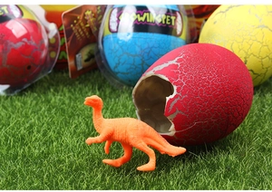 Close-up of a hatching dinosaur egg toy with an orange dinosaur on green grass surface