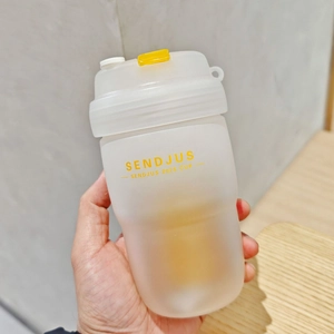 Close-up of hand holding a frosted transparent plastic tea cup with yellow SENDJUS logo