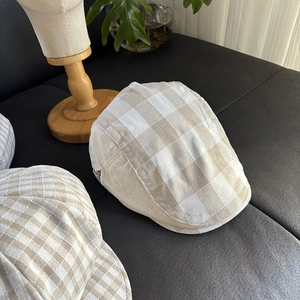 Detailed top view of a beige linen plaid flat cap on dark leather with wooden stand