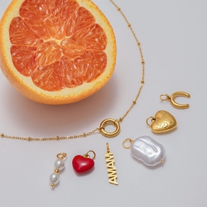 Macro shot of gold stainless steel necklace and baroque pearl charms on fresh orange