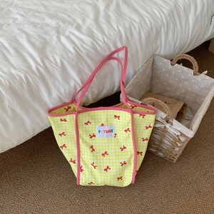 Yellow gingham canvas tote bag with red bow print and pink straps on a white bed