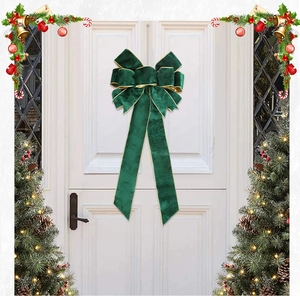 Close-up of a large green velvet Christmas bow with gold trim hanging on a white door