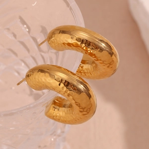 Macro shot of gold-plated hollow hoop earrings with hammered texture on a glass rim