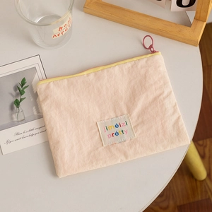 Pink fabric lipstick storage pouch with yellow zipper and colorful artistic label