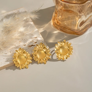 Vintage golden sunflower stud earrings in stainless steel on a rustic stone background